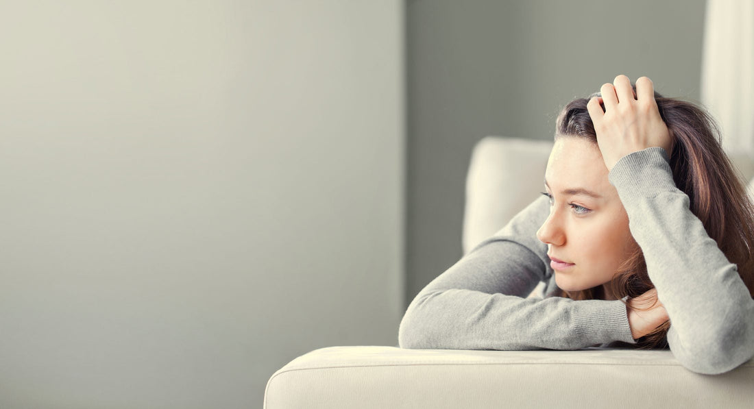 A woman rests her head on her arm while sitting on a couch, looking thoughtful