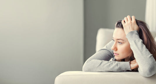 A woman rests her head on her arm while sitting on a couch, looking thoughtful