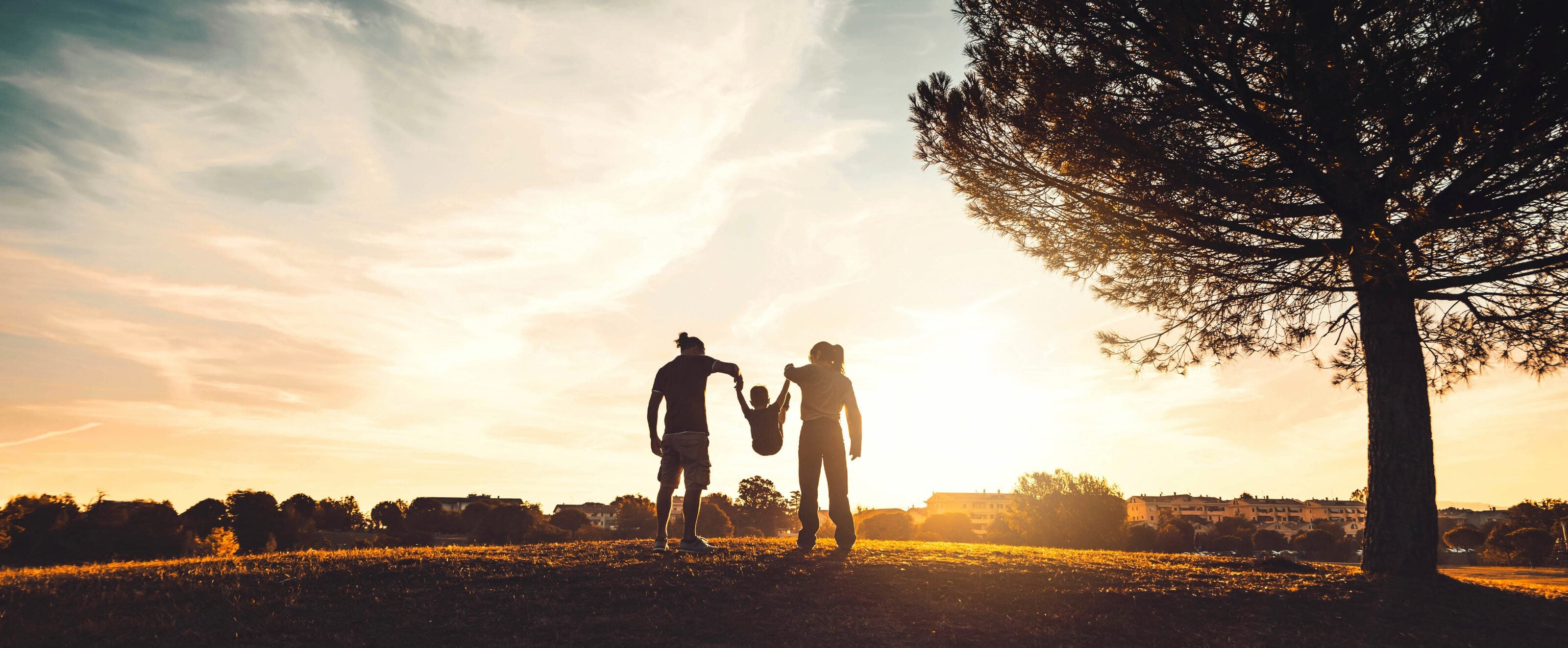 Two parents swinging their child by the hands at sunset in an open field