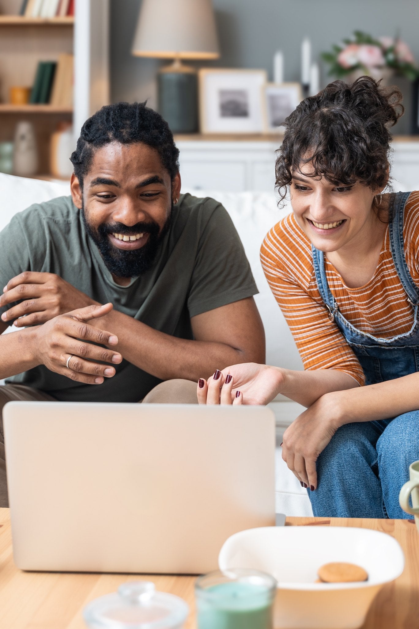 A couple sitting together on a sofa, smiling at a laptop during a virtual counseling session